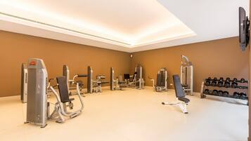 Uma academia com diversos equipamentos de exercício, um banco e uma estrutura com halteres.