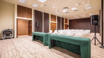 A conference room with a long table, rows of chairs, and a stage with a speaker.