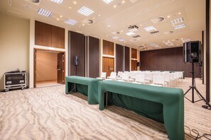 Un salón de conferencias con una larga mesa, filas de sillas y un escenario con un orador.