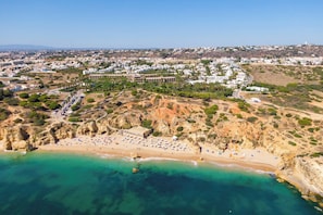 An aerial view of a coastal town with a beach, buildings, and a hilly landscape.