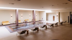 Un espacio de spa con un jacuzzi, sillones reclinables y una zona de estar con cojines amarillos.