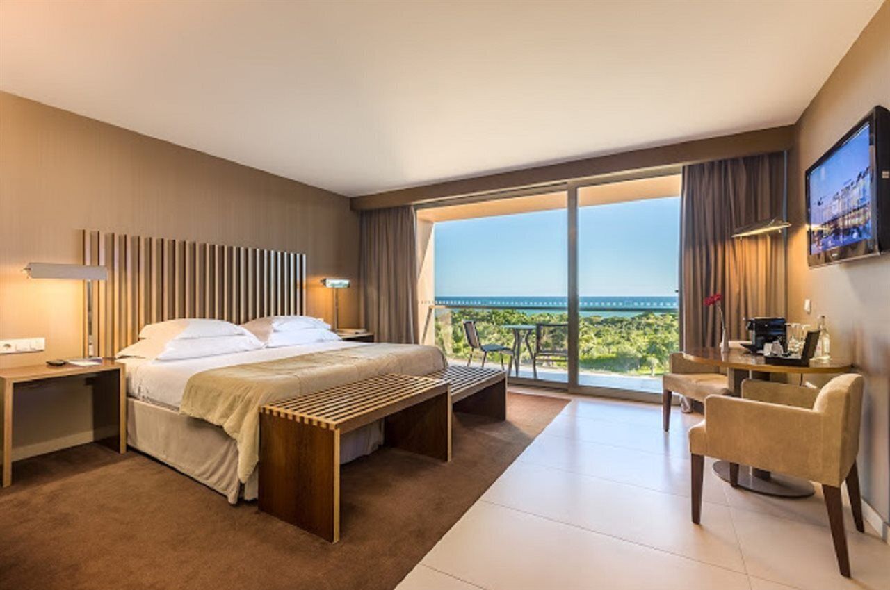 Hotelkamer met een bed, bureau, stoel, televisie en balkon met uitzicht op zee.