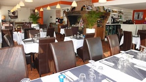 A restaurant with multiple dining tables, chairs, hanging pendant lights, and a brick wall with a fireplace. - Brit Hotel Hermes (Couchey)