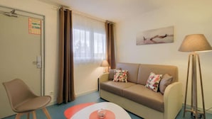 A room with a sofa, a chair, a lamp, and a painting on the wall. - Brit Hotel Hermes (Couchey)