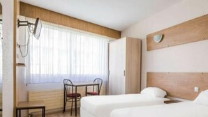 Hotellihuone, jossa on kaksi sänkyä, puinen pääty, pöytä tuoleineen ja ikkuna, jossa on verhot.