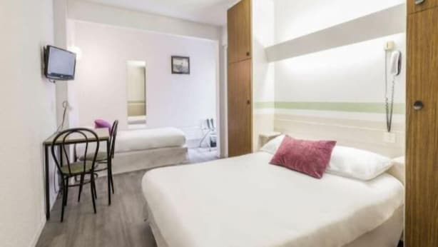 Hotellihuone, jossa on sänky, työpöytä tuolilla, televisio ja puhelin.