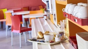 Un vassoio per la colazione con cornetti, caffè e condimenti su un tavolo bianco in un caffè con sedie arancioni e soffitto rosso.