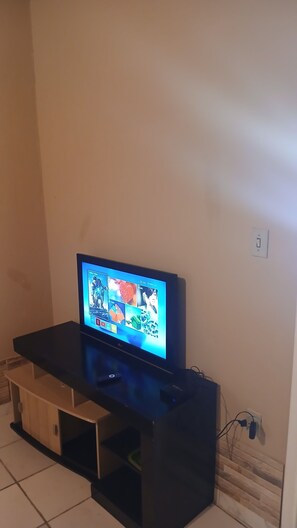 A television on a black stand with a wall socket nearby. - Country house in a gated community with a private lake, accommodates up to 20 people. (Ibiúna)