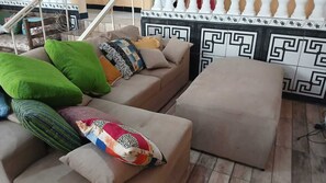 A living room with a sofa, ottoman, and a patterned wall. - Country house in a gated community with a private lake, accommodates up to 20 people. (Ibiúna)