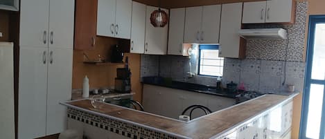 A kitchen with white cabinets, a black countertop, a window, and a tiled backsplash.