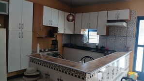 A kitchen with white cabinets, a black countertop, a window, and a tiled backsplash. - Country house in a gated community with a private lake, accommodates up to 20 people. (Ibiúna)
