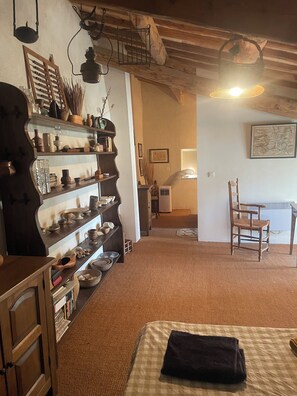 Ein gemütliches Zimmer mit Holzboden, einem Bett mit kariertem Überwurf, einem Sessel und einem Regal mit verschiedenen Gegenständen.