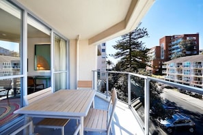 Un balcón con mesa y sillas, con vista a una calle con coches y edificios.