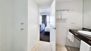 Et badeværelse på et hotel med brusebad, vask og spejl.
