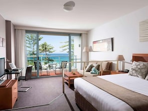 Habitación de hotel con cama, escritorio, silla, mesa, lámpara y vista al mar.