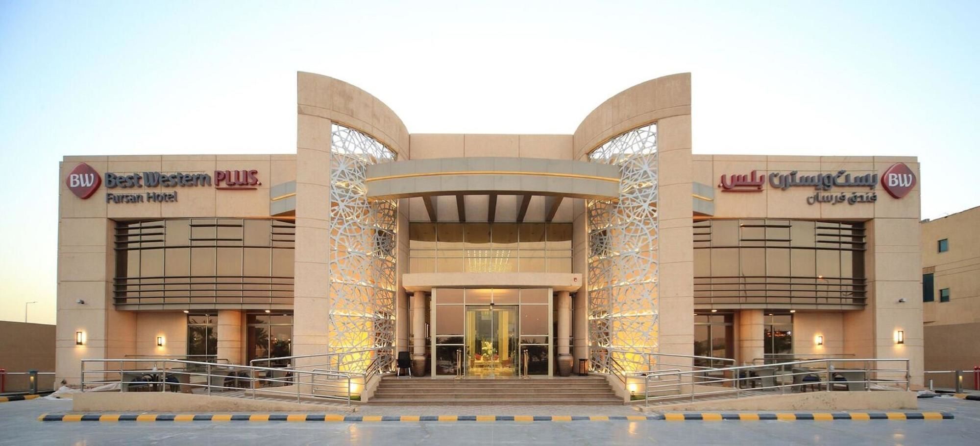 A hotel entrance with a modern design, featuring a central archway and two wings labeled 'Best Western PLUS' and 'Fursan Hotel'.