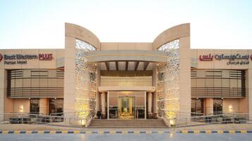 A hotel entrance with a modern design, featuring a central archway and two wings labeled 'Best Western PLUS' and 'Fursan Hotel'.