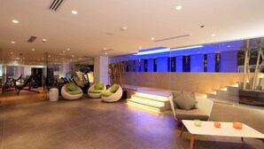Una palestra moderna con attrezzature per esercizi, zone relax e una scala che conduce a un balcone.