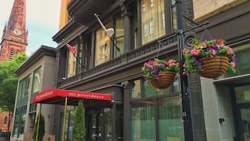 A hotel with a red awning, hanging flower baskets, and a clock tower in the background.