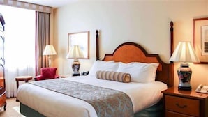 Une chambre d’hôtel avec un grand lit, des tables de chevet, un fauteuil rouge et une lampe.