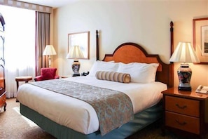 Une chambre d’hôtel avec un grand lit, des tables de chevet, un fauteuil rouge et une lampe.