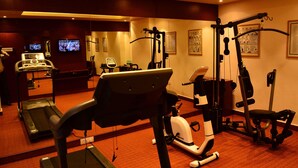 A hotel fitness center with cardio equipment, weight machines, and a television displaying a sports event. - Sagar Sona (Lucknow)