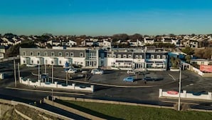 A parking lot with multiple cars, a building with a flat roof, and a clear sky. - The White Sands Hotel Portmarnock (Portmarnock)