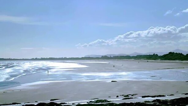 A beach with a wide sandy area, a rocky foreground, and distant mountains under a clear sky. - The White Sands Hotel Portmarnock (Portmarnock)