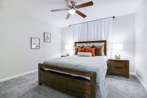 Une chambre à coucher comprenant un lit, deux tables de chevet, un ventilateur de plafond et deux lampes fixées au mur.