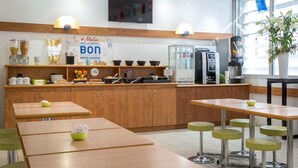 Een café met houten tafels en groene krukken, een koffieapparaat, en een bord waarop 'Malin Bonjour' staat.
