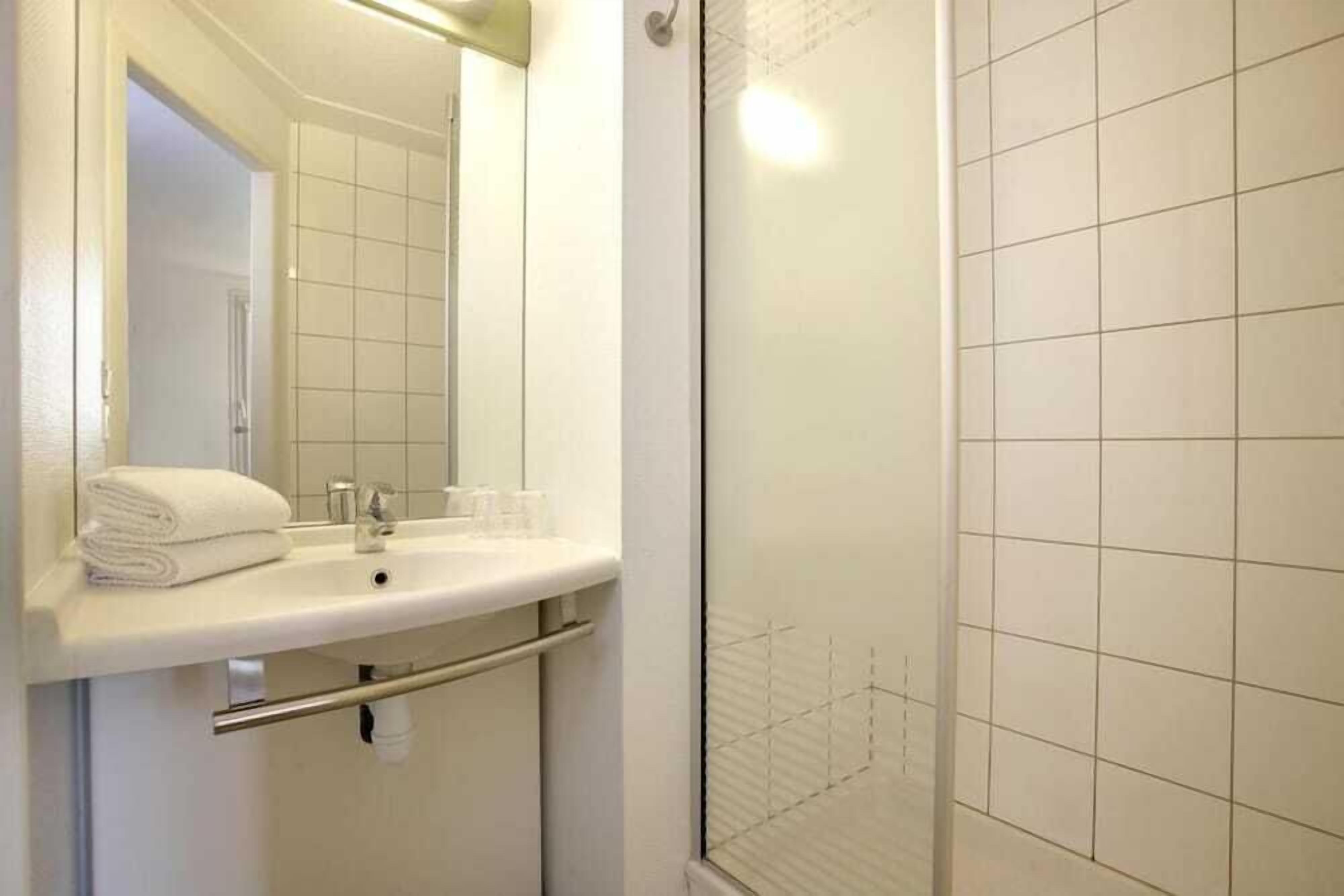 Une salle de bain avec un lavabo blanc, un miroir et un espace douche.