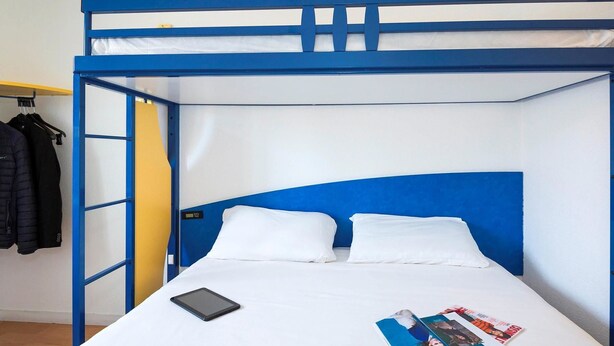 Een stapelbed met een blauw frame, witte beddengoed en een tablet op het onderste bed.
