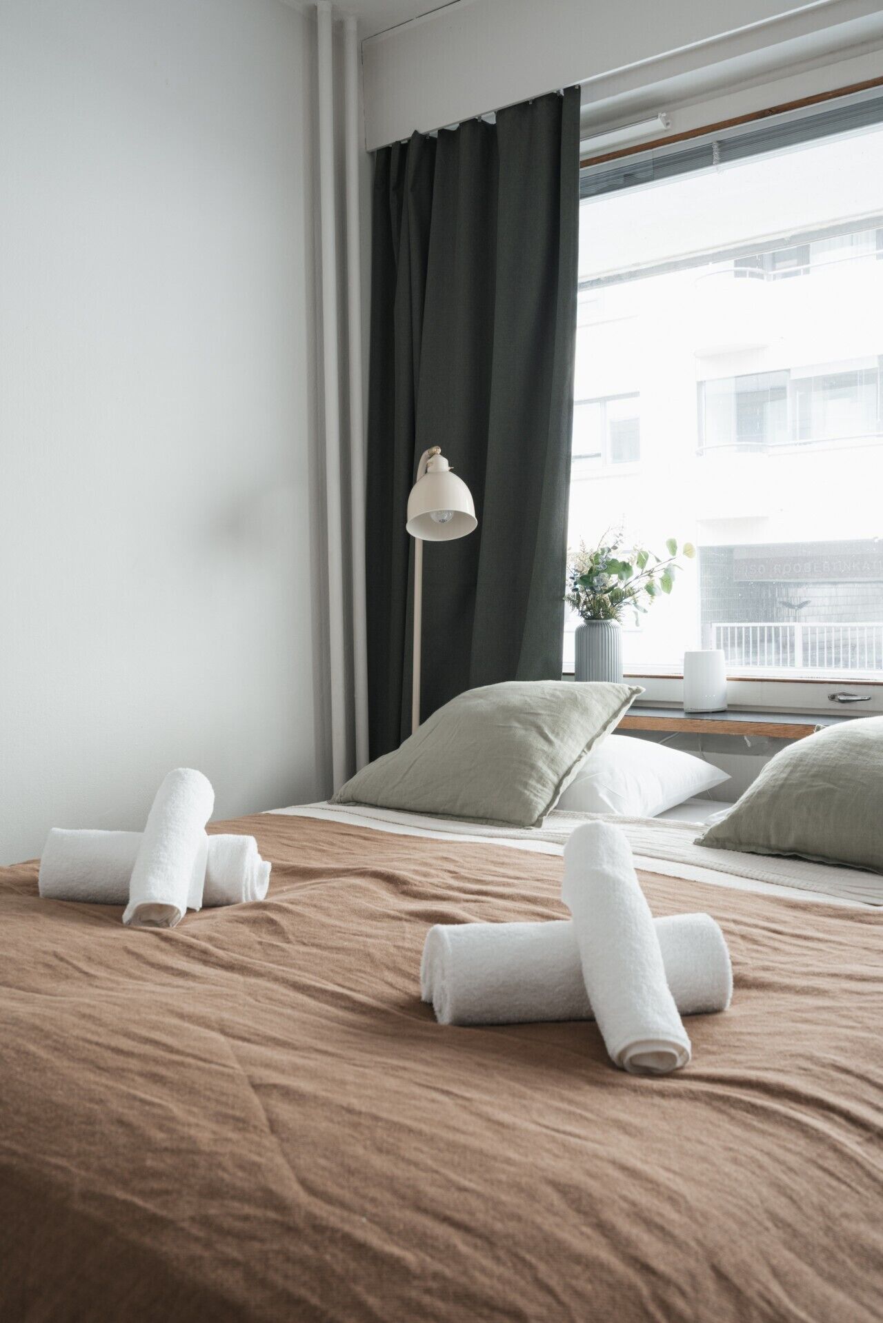 Een hotelkamer met een bed, kussens, een lamp en een raam met gordijnen.