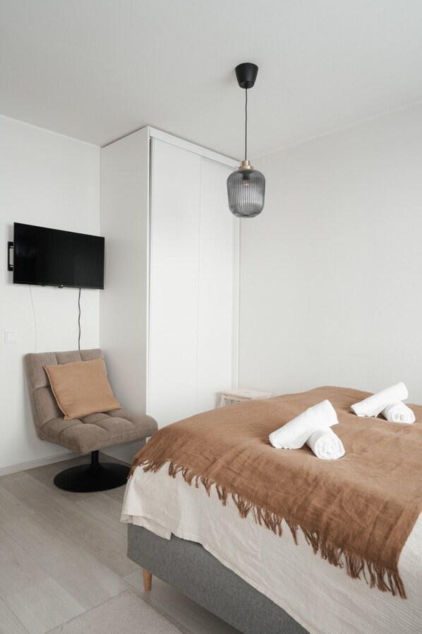 Un dormitorio moderno con cama, una silla, televisión y lámpara colgante.