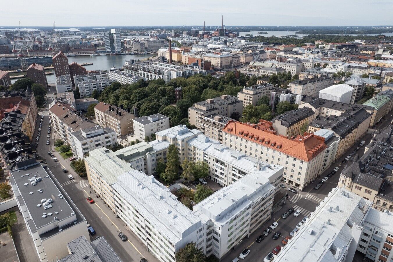Eine Stadtansicht mit einer Mischung aus moderner und traditioneller Architektur, darunter ein markantes Gebäude mit rotem Dach und ein großer, offener Platz im Vordergrund.