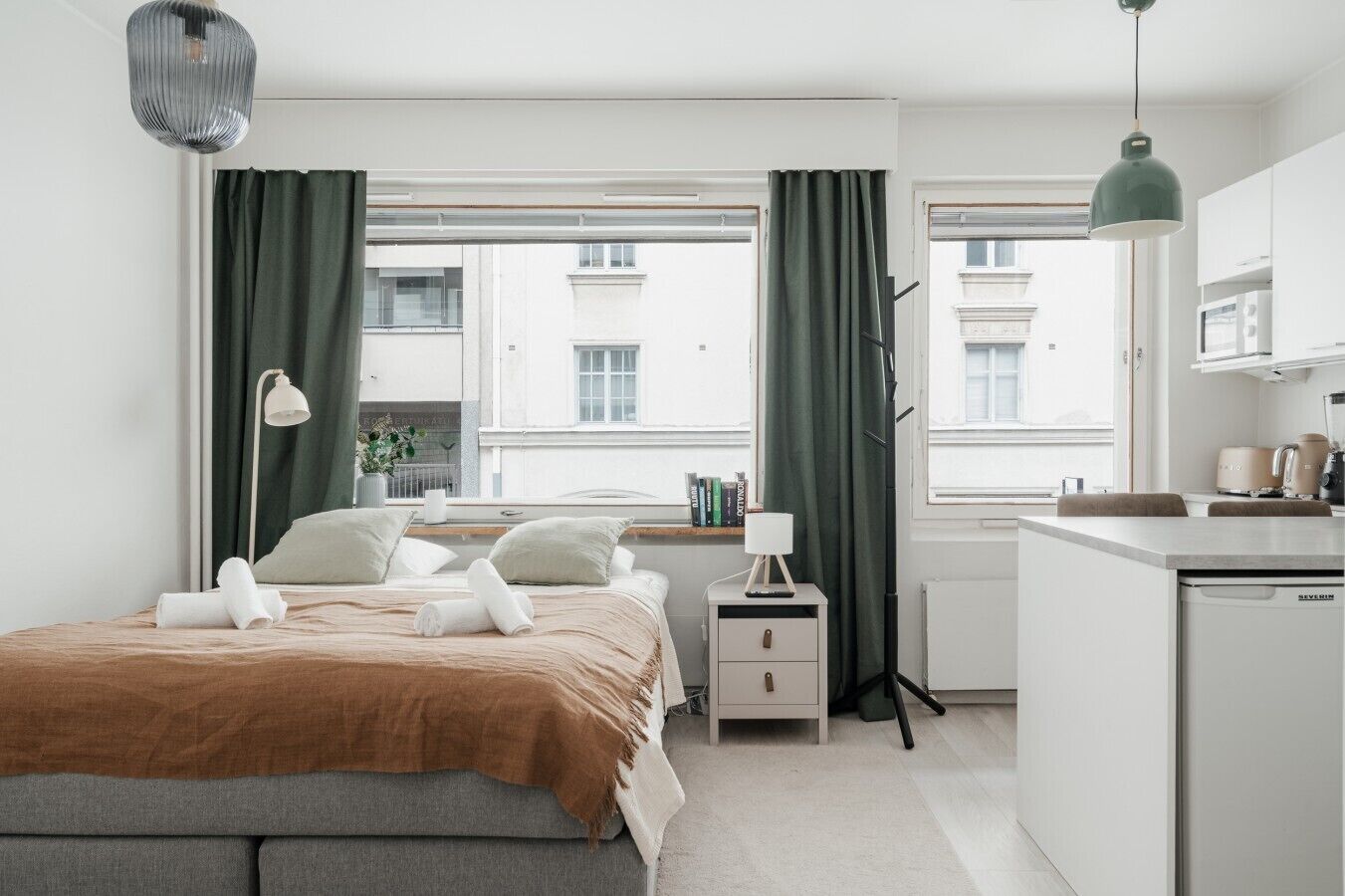 A modern bedroom with a bed, bedside table, lamp, and a view of the city through large windows.