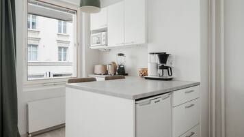 A modern kitchen with white cabinets, a countertop, a coffee maker, and a window with a view of buildings.