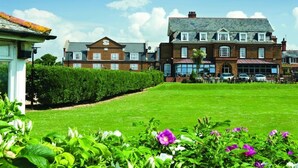 A large building with a symmetrical facade, multiple windows, and a well-maintained lawn with flowers. - Le Strange Arms Beachside Hotel & Lodges (Hunstanton)