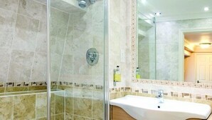 A modern bathroom with a glass-enclosed shower, a sink, and wooden cabinets. - Le Strange Arms Beachside Hotel & Lodges (Hunstanton)
