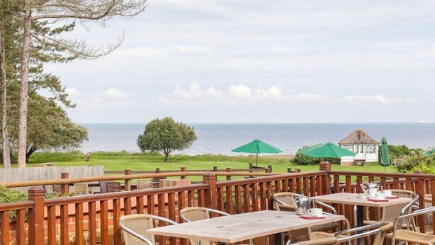 An outdoor dining area with tables and chairs, a wooden fence, and a view of the sea. - Le Strange Arms Beachside Hotel & Lodges (Hunstanton)