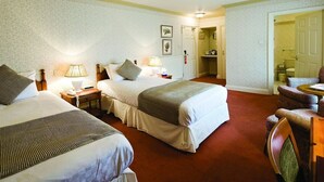 A hotel room with two beds, a sitting area with a chair, a lamp, and a small table. - Le Strange Arms Beachside Hotel & Lodges (Hunstanton)