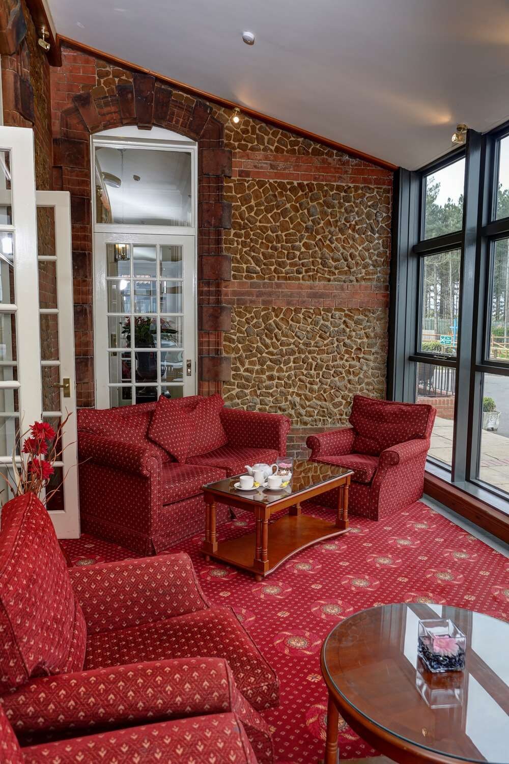 Una habitación acogedora con muebles de diseño rojo, una pared de piedra y un ventanal grande.