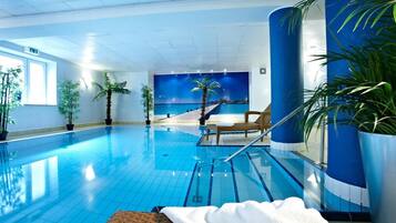 Ein Innenpool mit klaren blauen Fliesen, eine Lounge-Bereich mit einem Sessel und einem Handtuch sowie Topfpflanzen.