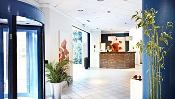Eine Hotelhalle mit einer Rezeption, einem großen Fenster und einer Zimmerpflanze.