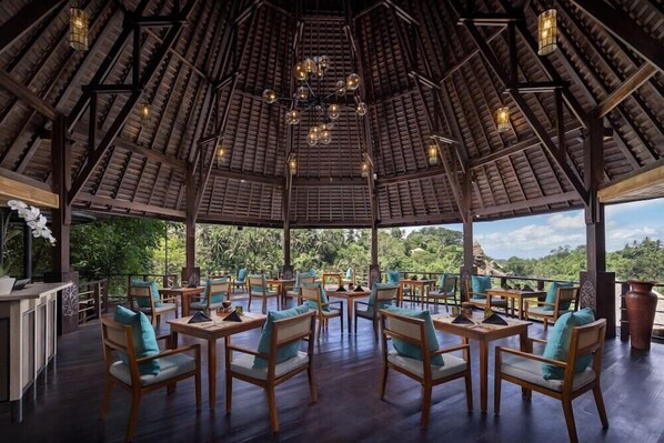 A covered outdoor dining area with wooden furniture and a view of the surrounding landscape. - The Kayon Valley Resort (Ubud)