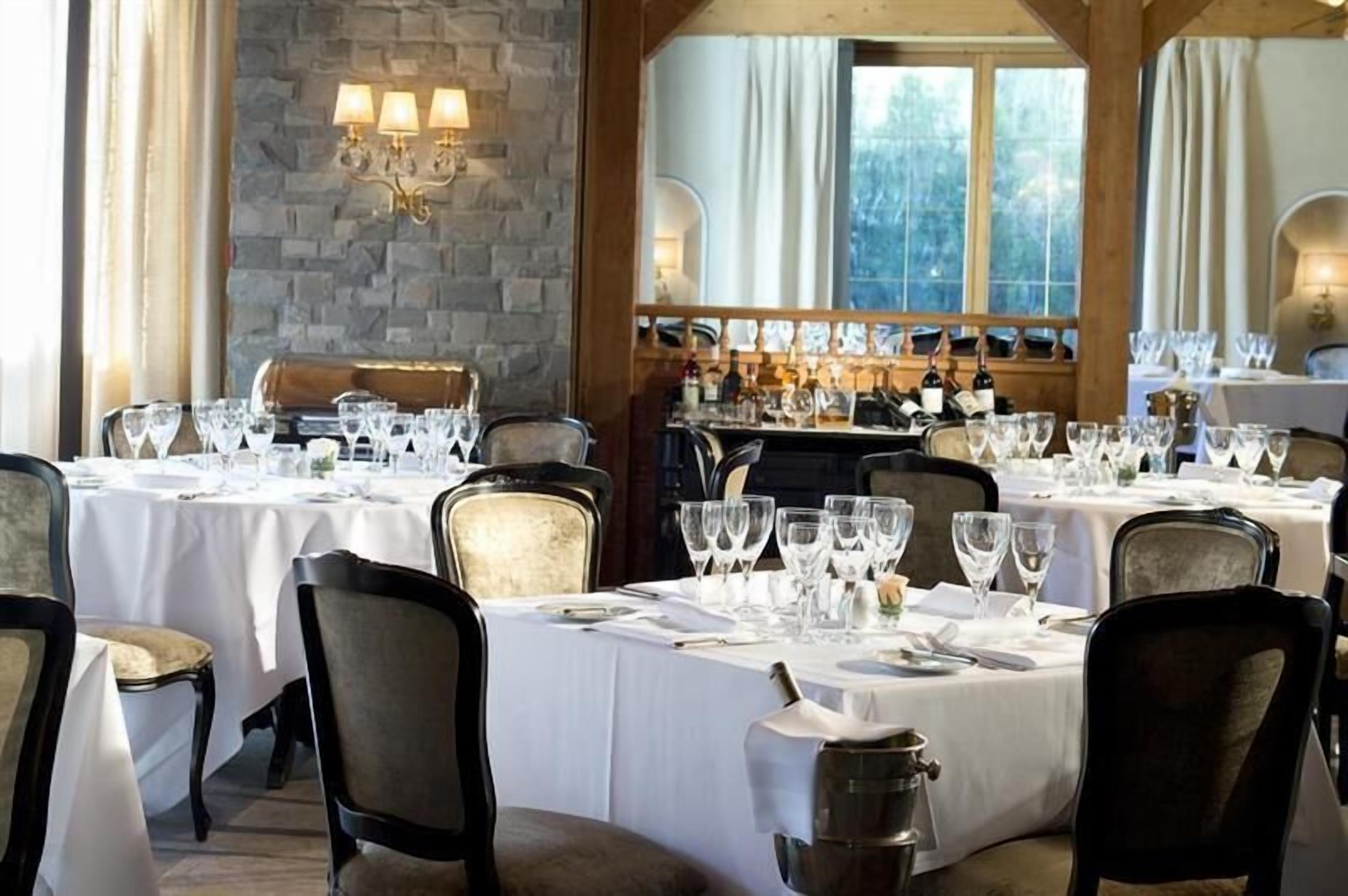 A restaurant with multiple tables set for dining, featuring a stone wall and wooden beams.