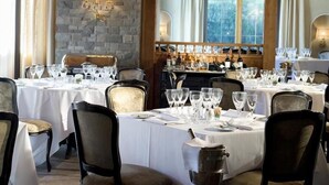 A restaurant with multiple tables set for dining, featuring a stone wall and wooden beams.