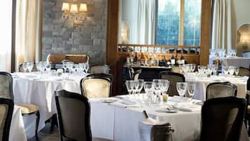 A restaurant with multiple tables set for dining, featuring a stone wall and wooden beams.