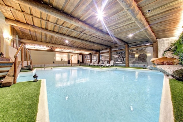 An indoor swimming pool with a wooden ceiling, a small staircase, and lounge chairs. - Hotel Fluela Davos (Davos)