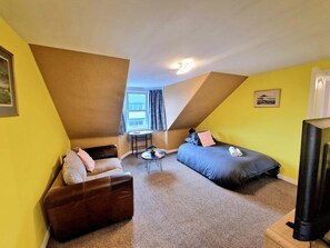 Ein kleiner, dreieckiger Raum mit einem Bett, einer Couch, einem Tisch und einem Fernseher.